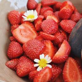 Bowl of sliced strawberries with white flowers on top.