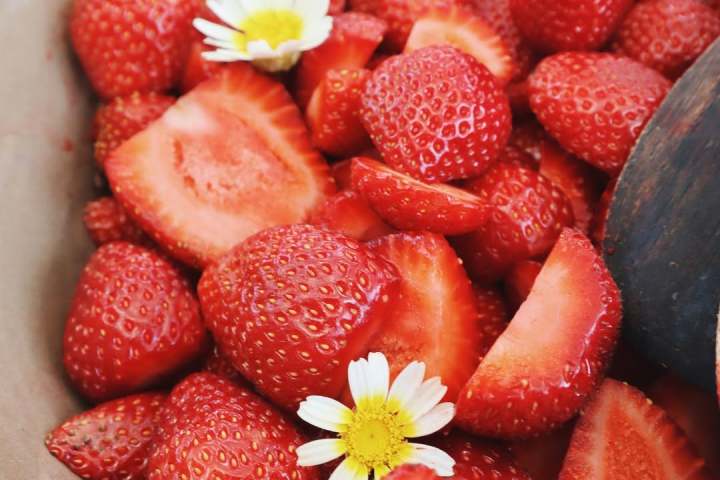 Bowl of sliced strawberries with white flowers on top.
