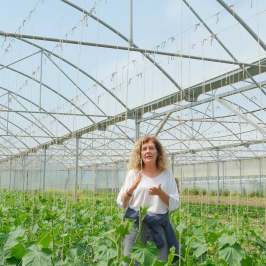 Person standing in a greenhouse surrounded by plants.