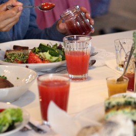 People dining, serving jam, with salads and red juice on a table.