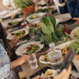 Group of people dining at a table with plates of salad and leafy greens.