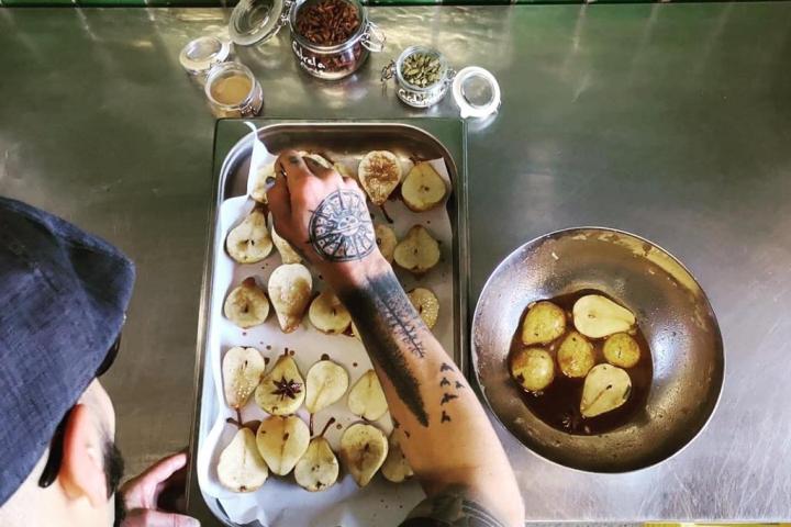 Chef preparing baked pears with spices on a tray in a kitchen.