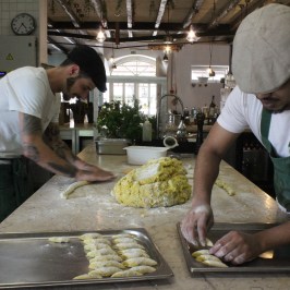 Two people preparing dough in a rustic kitchen setting.
