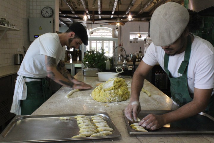 Two people preparing dough in a rustic kitchen setting.