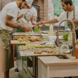 Chefs preparing food in a rustic kitchen with green tiles.
