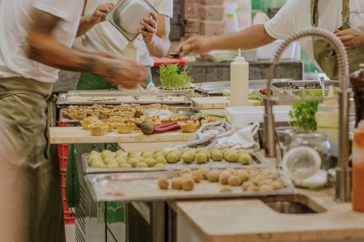 Chefs preparing food in a rustic kitchen with green tiles.