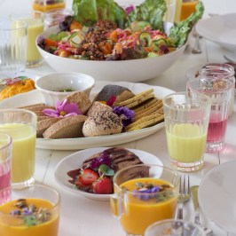 A colorful brunch table with dishes of salads, desserts, juices, and vibrant decorations.