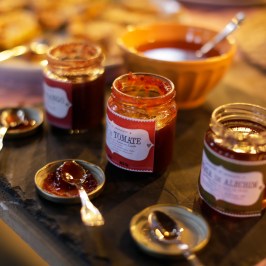 Jars of jam with spoons on lids next to a bowl on a table.
