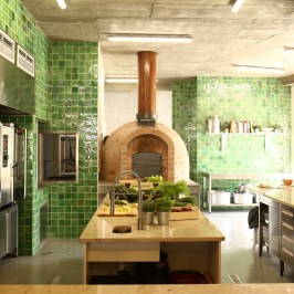 Spacious kitchen with green tiles, pizza oven, and countertop filled with herbs and cookware.