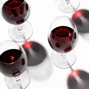 Five wine glasses with red wine on a white background, casting shadows.