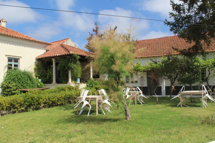 Sunny garden with tables and chairs near a house with red-tiled roof.