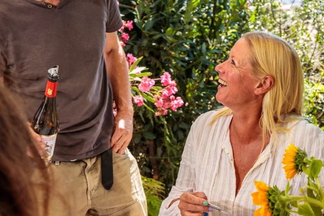 Man with wine and woman laughing at outdoor meal with flowers.