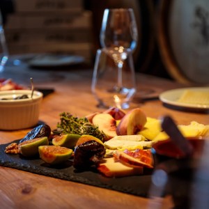 Gourmet cheese and fruit platter on wooden table with wine glasses.