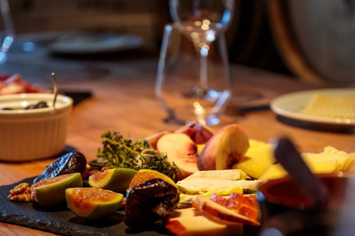 Gourmet cheese and fruit platter on wooden table with wine glasses.