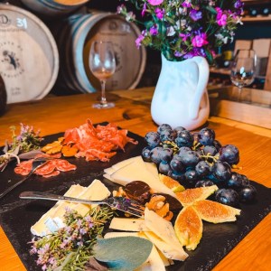 Cheese and charcuterie board with figs and grapes; flowers in vase nearby.