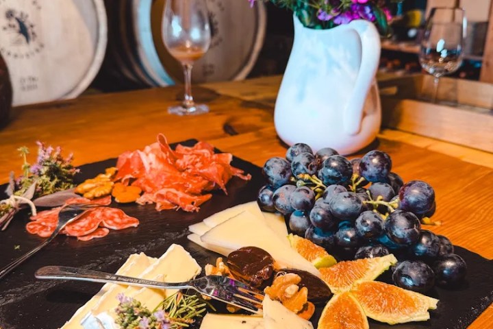 Cheese and charcuterie board with figs and grapes; flowers in vase nearby.
