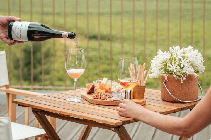 Outdoor table with wine, nuts, cheese, flowers and a scenic vineyard view.