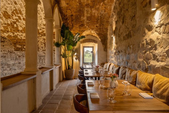 Warm-toned rustic dining area with stone walls, arches, and wooden tables set for guests.