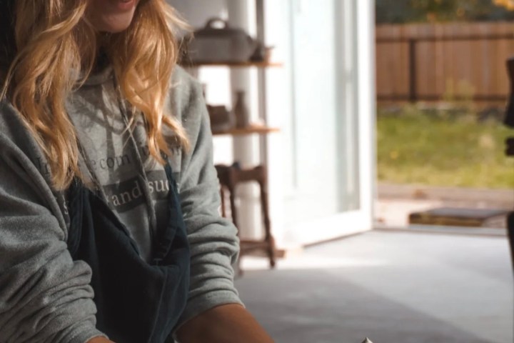 Smiling woman potter shaping clay on a wheel in a sunlit room with open door.