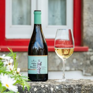 Wine bottle and glass on stone ledge, red window frame, daisies in foreground.