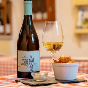 Wine bottle, glass, and bowl of snacks on a checkered tablecloth.