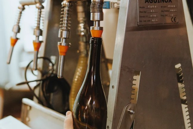 Person placing a bottle under an industrial liquid filling machine.
