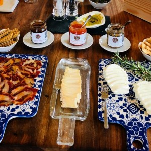 Cheese and charcuterie boards with breads and spreads on a wooden table.