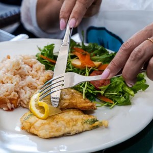 Person eating fish with lemon, rice, and salad.