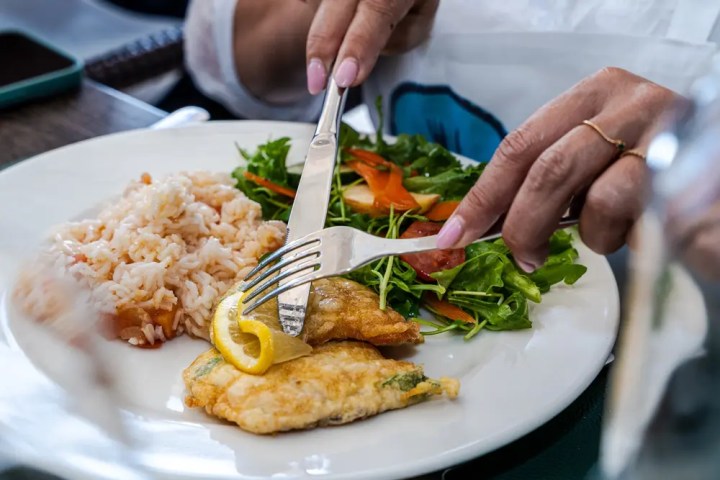 Person eating fish with lemon, rice, and salad.