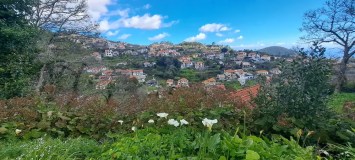 A scenic view of a hillside village with white houses and red roofs under a blue sky with clouds.