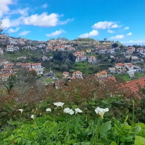 A scenic view of a hillside village with white houses and red roofs under a blue sky with clouds.