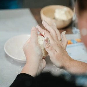 Person shaping dough with hands over a table.