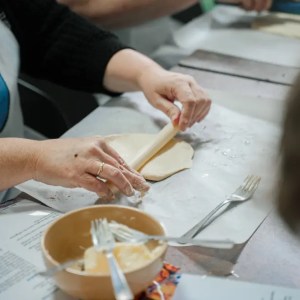 Person in apron rolling dough with rolling pin on a table.