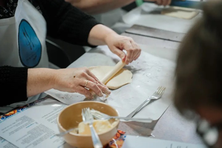 Person in apron rolling dough with rolling pin on a table.