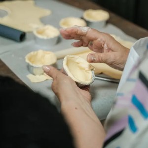 Person shaping dough into small baking tins on a table.