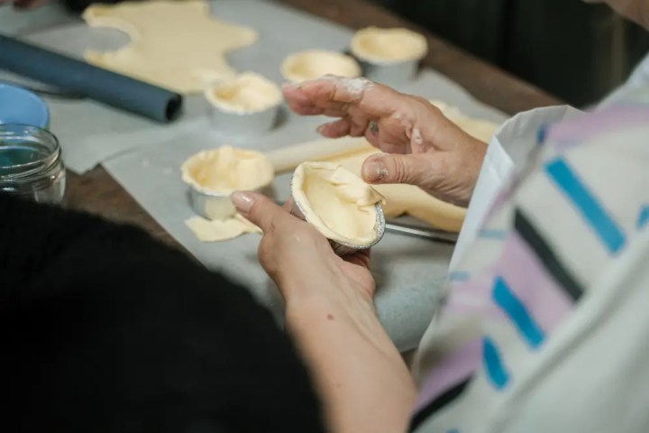 Person shaping dough into small baking tins on a table.