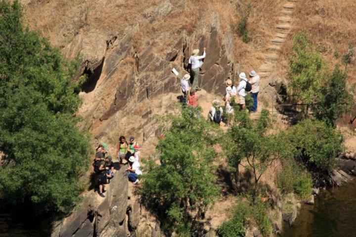 Group of people standing on rocky riverbank with trees nearby.