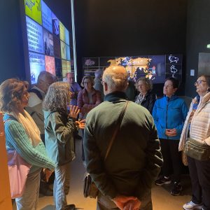 People gathered indoors, viewing multimedia displays on the wall.