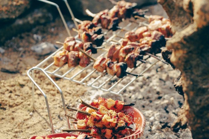 Skewers of meat and vegetables cooking on a metal grill over coals.