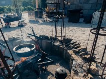 Outdoor fire pit with cooking equipment and vineyard in the background.