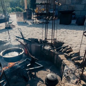 Outdoor fire pit with cooking equipment and vineyard in the background.