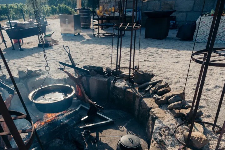 Outdoor fire pit with cooking equipment and vineyard in the background.