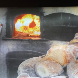 Loaves of bread cooling near a traditional stone oven with a fire inside.