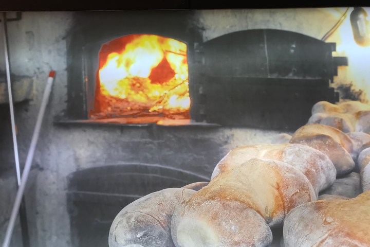 Loaves of bread cooling near a traditional stone oven with a fire inside.