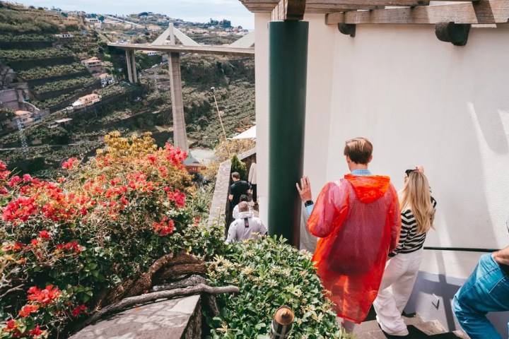 Tourists in bright clothes walking down outdoor stairs with a scenic view of a bridge and lush hillsides.