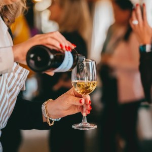 Person pouring white wine into a glass at a social event.