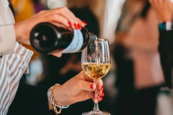 Person pouring white wine into a glass at a social event.