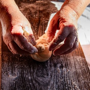 Hands kneading dough on a dark wooden surface.