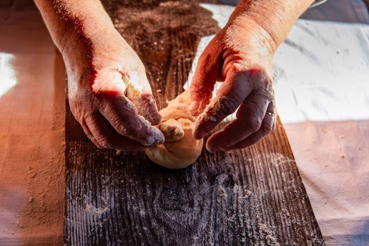 Hands kneading dough on a dark wooden surface.