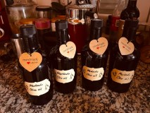 Four dark bottles of handmade olive oil with heart tags on a kitchen counter.
